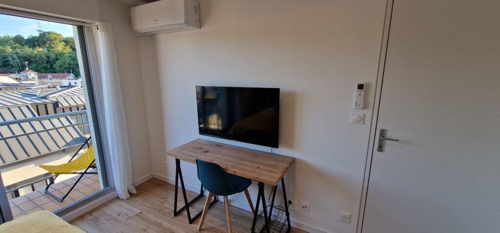 Une table et une chaise devant une TV affixée à l'un des murs de la pièce. 